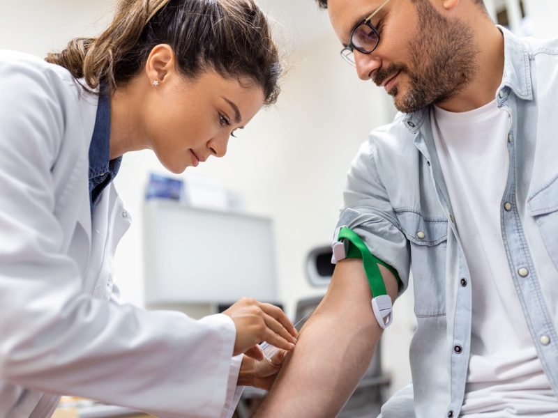 Friendly hospital phlebotomist collecting blood sample from patient in lab. Preparation for blood test by female doctor medical uniform on the table in white bright room